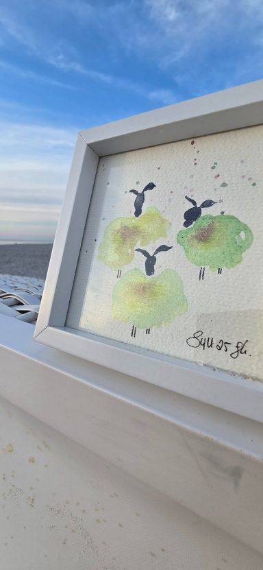Konfettischafe Aquarell Drei grüne Schafe mit schwarzen Köpfen auf einem Künstlerbild im Freien.