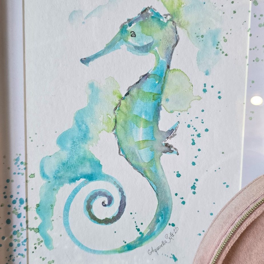 Rahmen mit Aquarell eines Wals, umgeben von Gras im Sand.