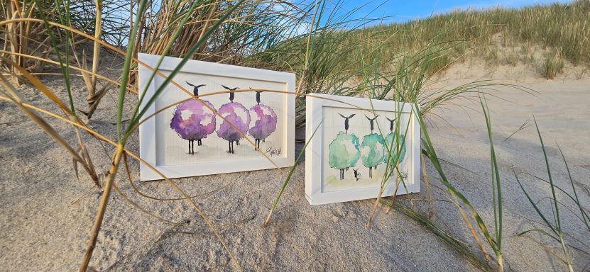 Wollschafe Aquarell Zwei bemalte Eier in lilarot und grün liegen im Sand, umgeben von Gras.