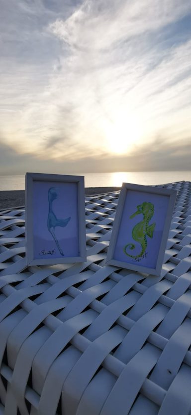 Sylt und Seepferdchen Zwei Bilderrahmen mit den Buchstaben "L" und einem geschwungenen Zeichen vor einem Sonnenuntergang.
